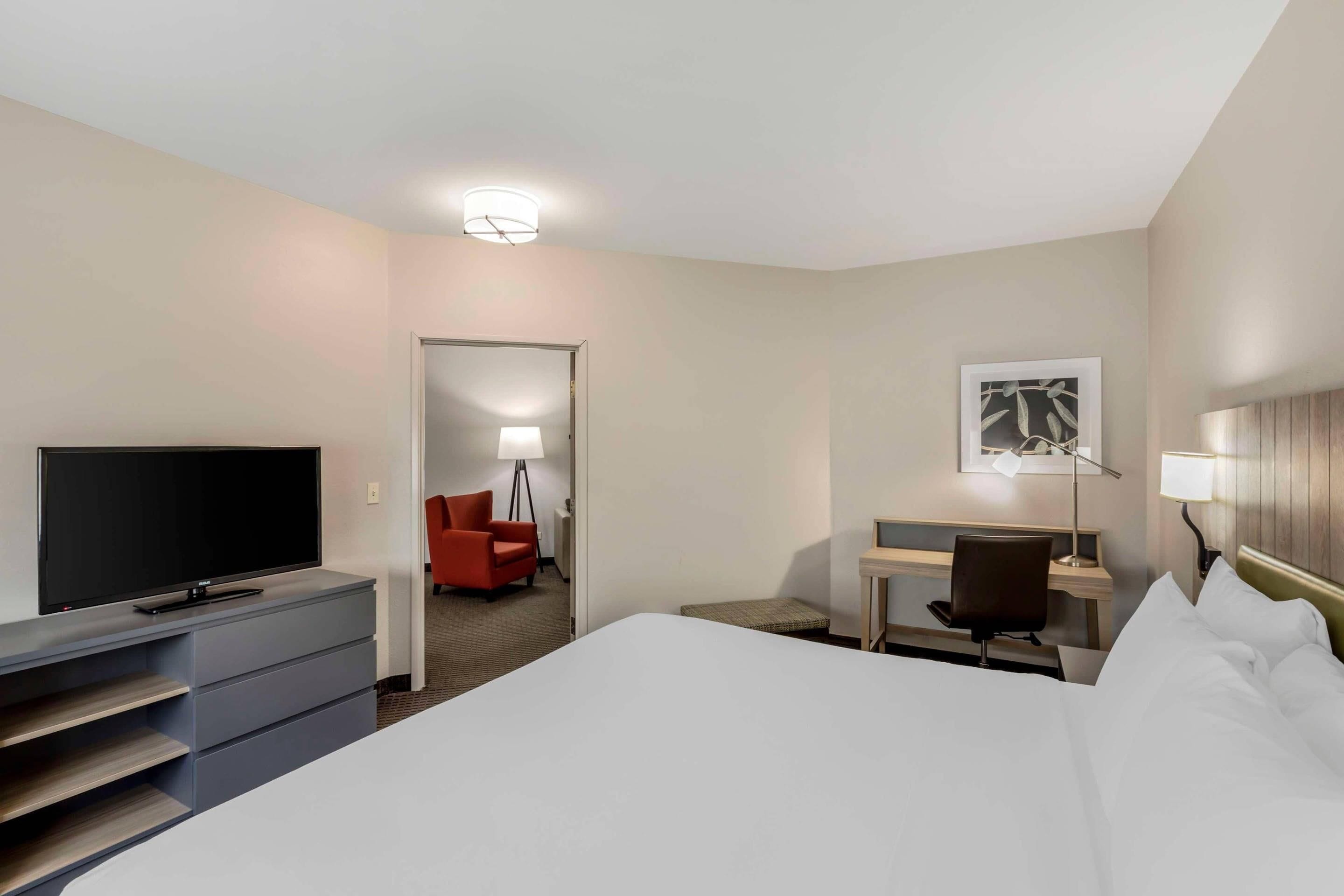 A hotel room with a bed, a desk, a chair, a television, and a lamp.