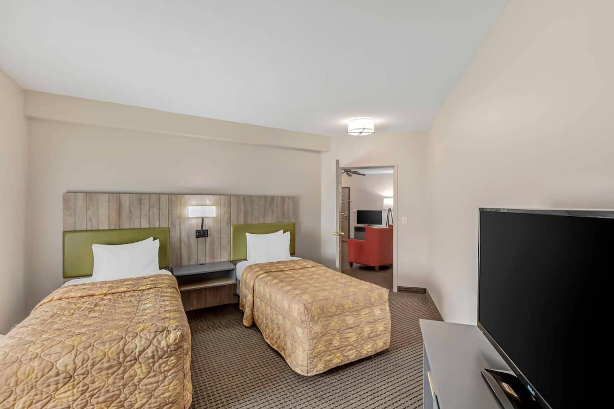 A hotel room with two beds, a TV, a desk, and a mirror.