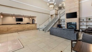 A spacious lobby with a reception desk, a staircase, a grey sofa, and a TV mounted on the wall. - Country Inn & Suites by Radisson, Elk Grove Village/Itasca (Elk Grove Village)