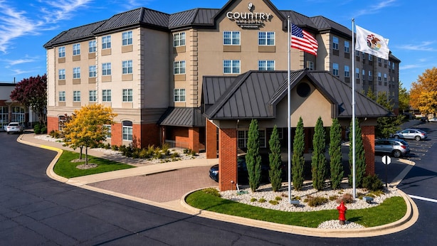 A multi-story hotel with a prominent American flag, a sign for 'Country Inn & Suites by Radisson,' and a landscaped entrance area.