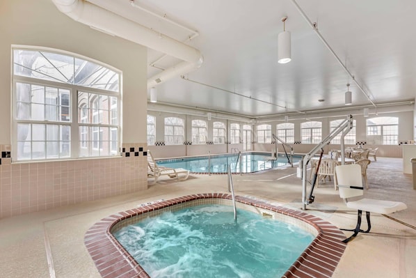 A large indoor swimming pool with a hot tub, surrounded by lounge chairs and a staircase.