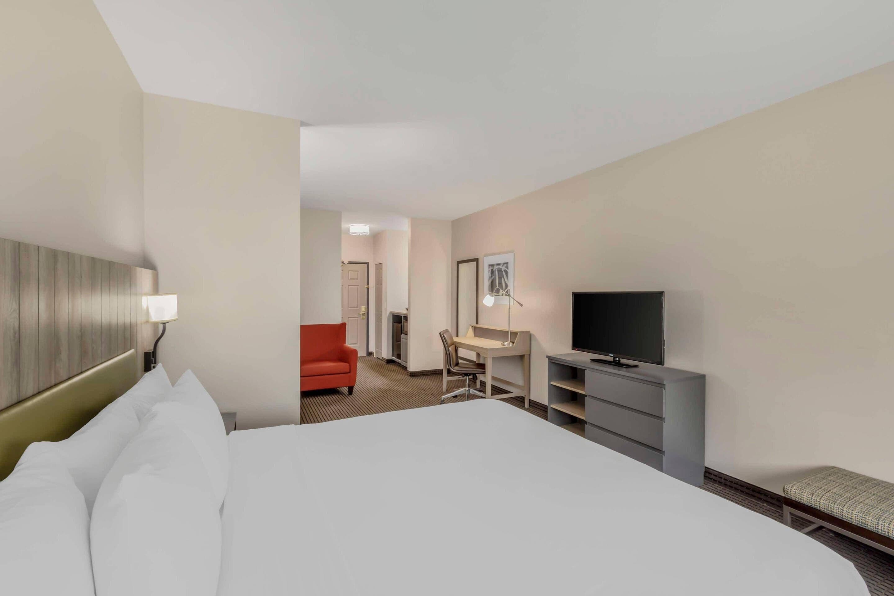 Una habitación de hotel con cama, escritorio, televisor y una silla roja.