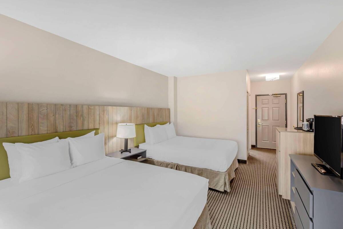 A hotel room with two beds, a desk with a television, and a door leading to a bathroom.