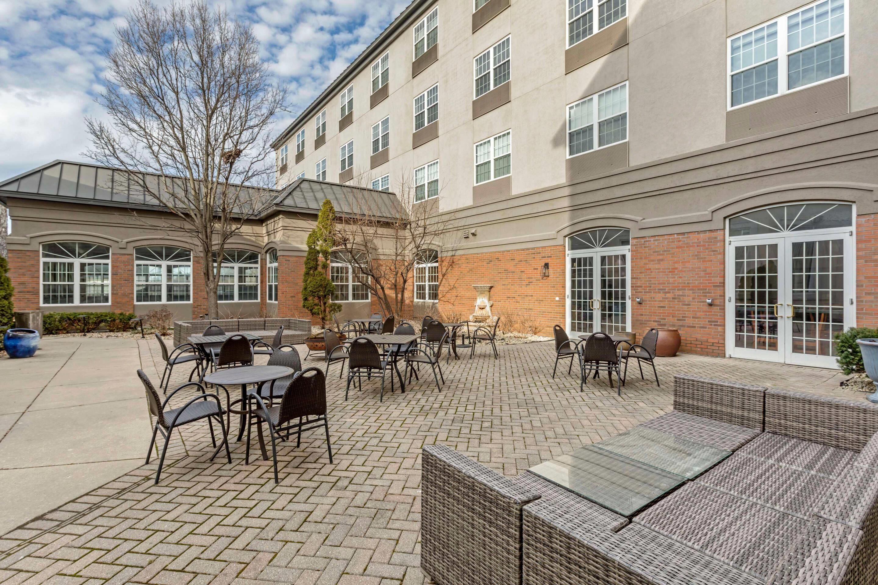 A courtyard with outdoor seating, a brick building, and a tree.