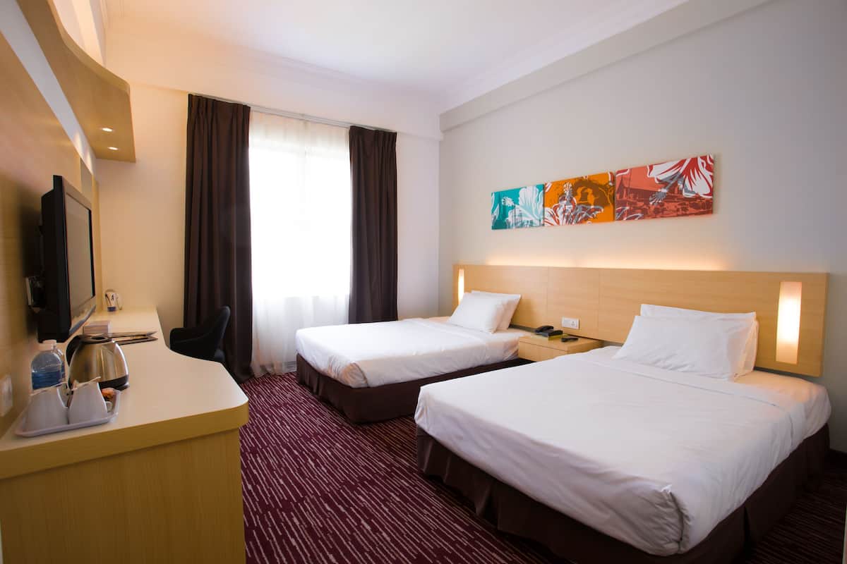 A hotel room with two beds, a desk with a television, and a window with curtains.