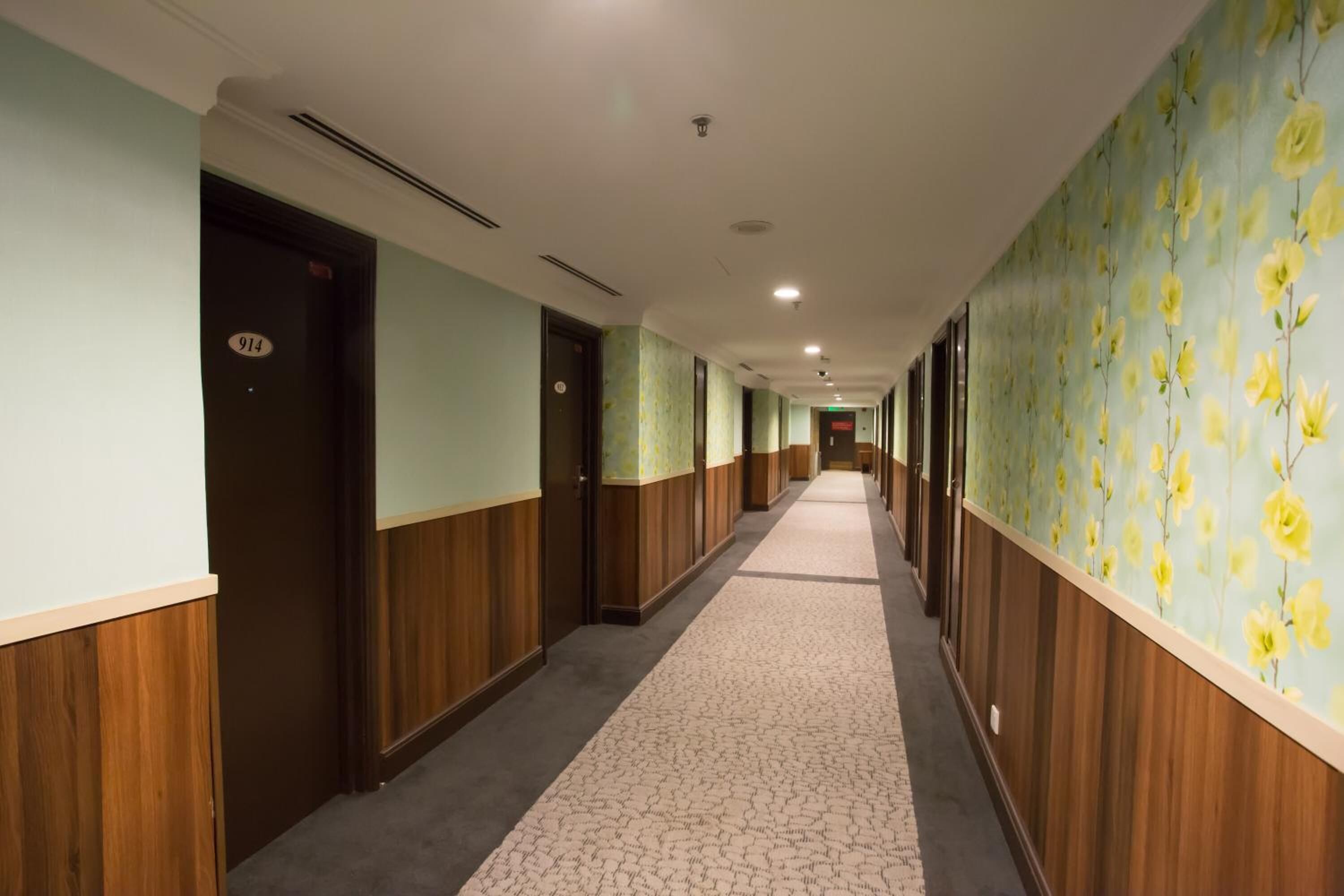 Un pasillo con puertas a la izquierda, una alfombra estampada y papel tapiz floral a la derecha.