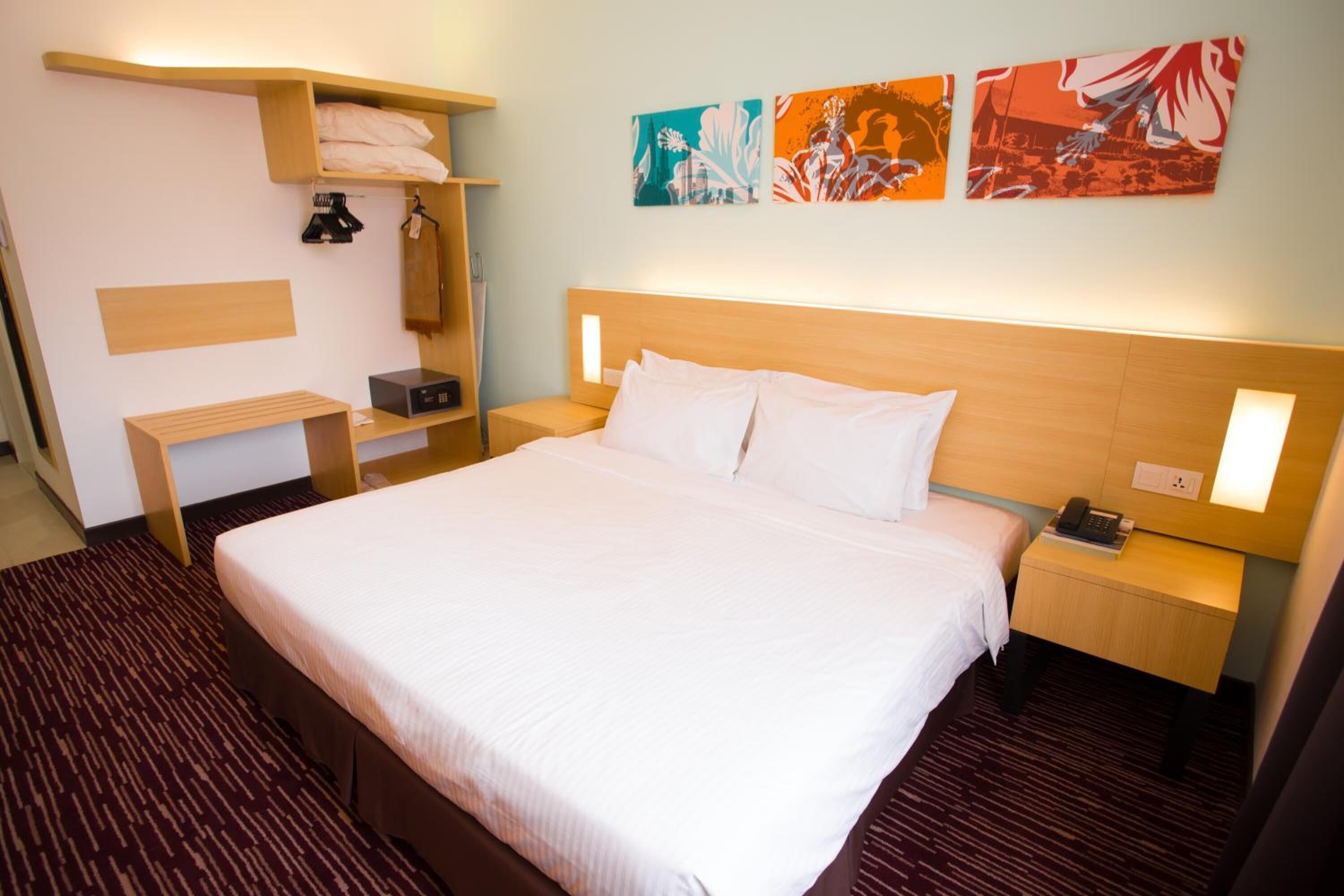 Habitación de hotel con una cama grande, mesitas de noche, un armario y cuadros en la pared.