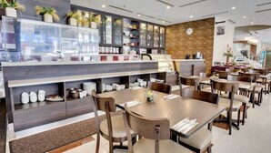 Um restaurante moderno com uma área de jantar central, mesas redondas e cadeiras de madeira, rodeada por vitrines de vidro com diversos objetos.