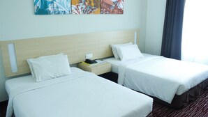 Quarto de hotel com duas camas de solteiro, mesa de cabeceira, luminária e um quadro na parede.