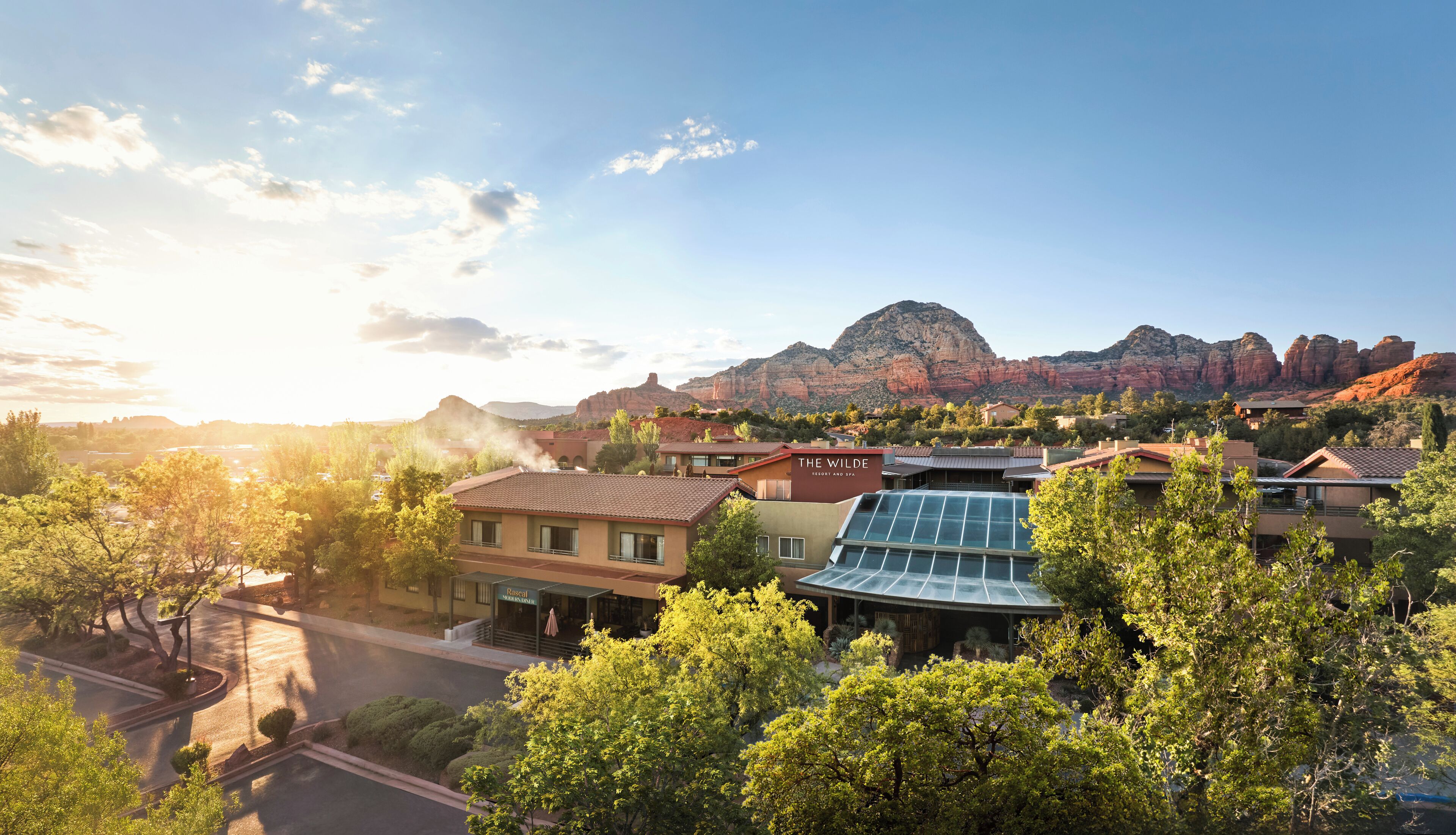 Un complexe hôtelier situé au pied d’une montagne, avec un bâtiment doté d’un toit recouvert de panneaux solaires et d’une enseigne indiquant : « The Wilde Resort and Spa ».