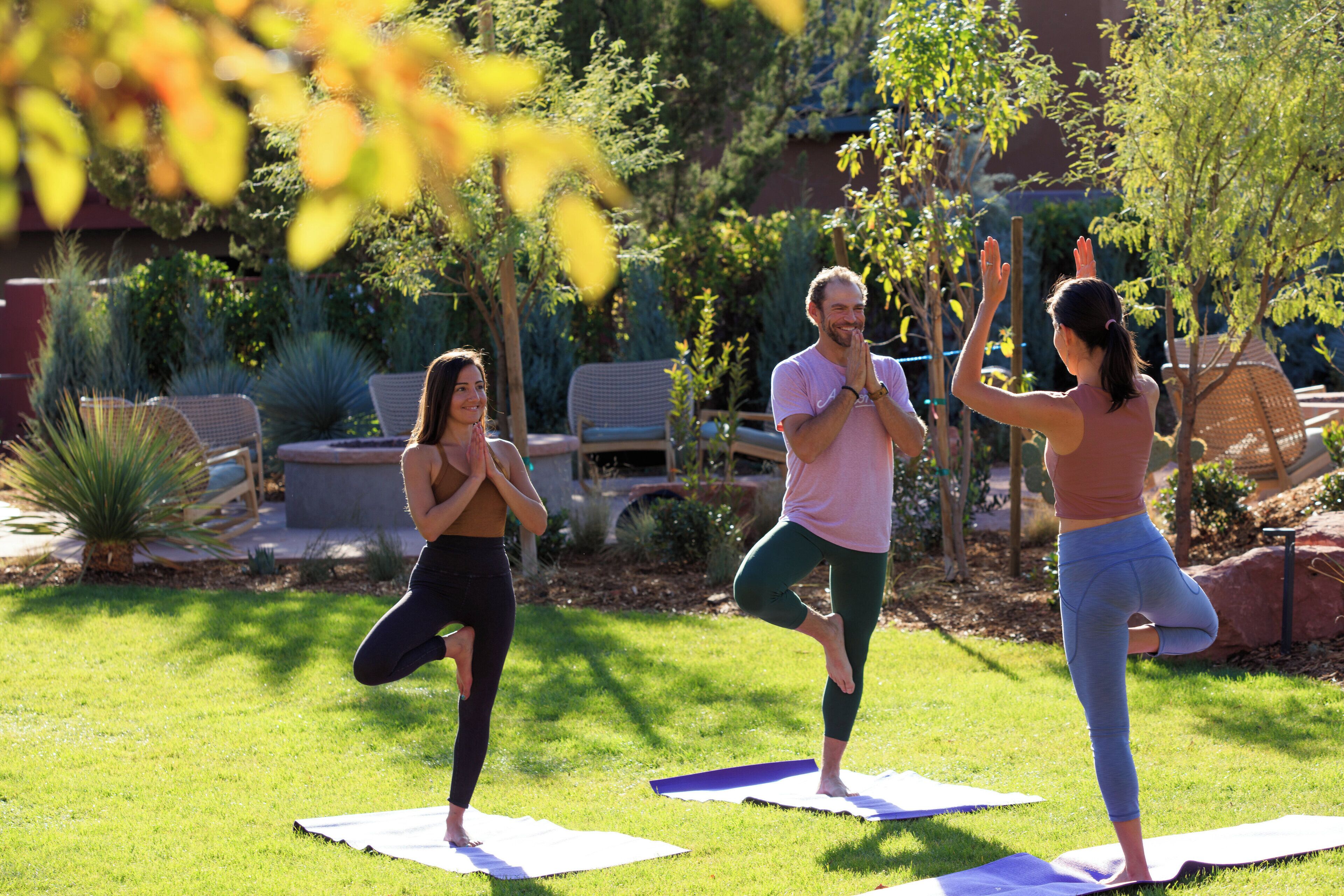 Trois personnes pratiquent le yoga en plein air sur des tapis.