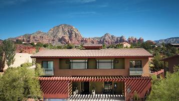 A two-story building with a red-tiled roof, a covered patio with outdoor seating, and a view of red rock formations in the background.