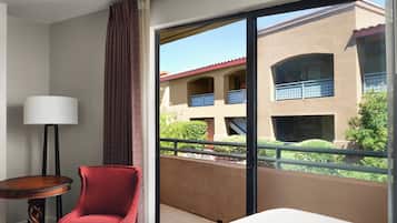 Une chambre d’hôtel avec un lit, une chaise rouge, une petite table et une grande fenêtre donnant sur un immeuble doté de balcons.