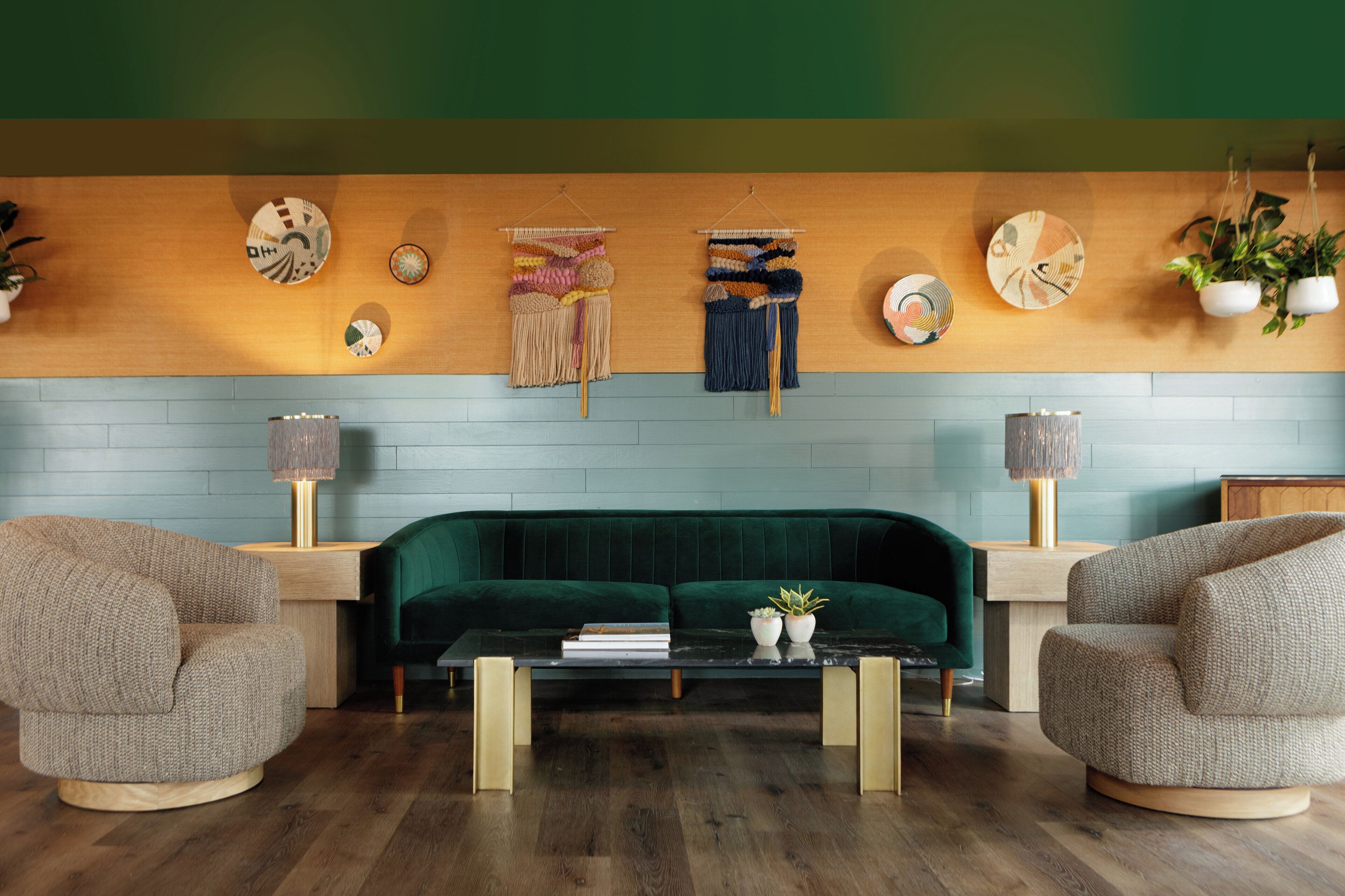A modern living room with a green sofa, two armchairs, a coffee table, and wall decor including plates and hanging plants.