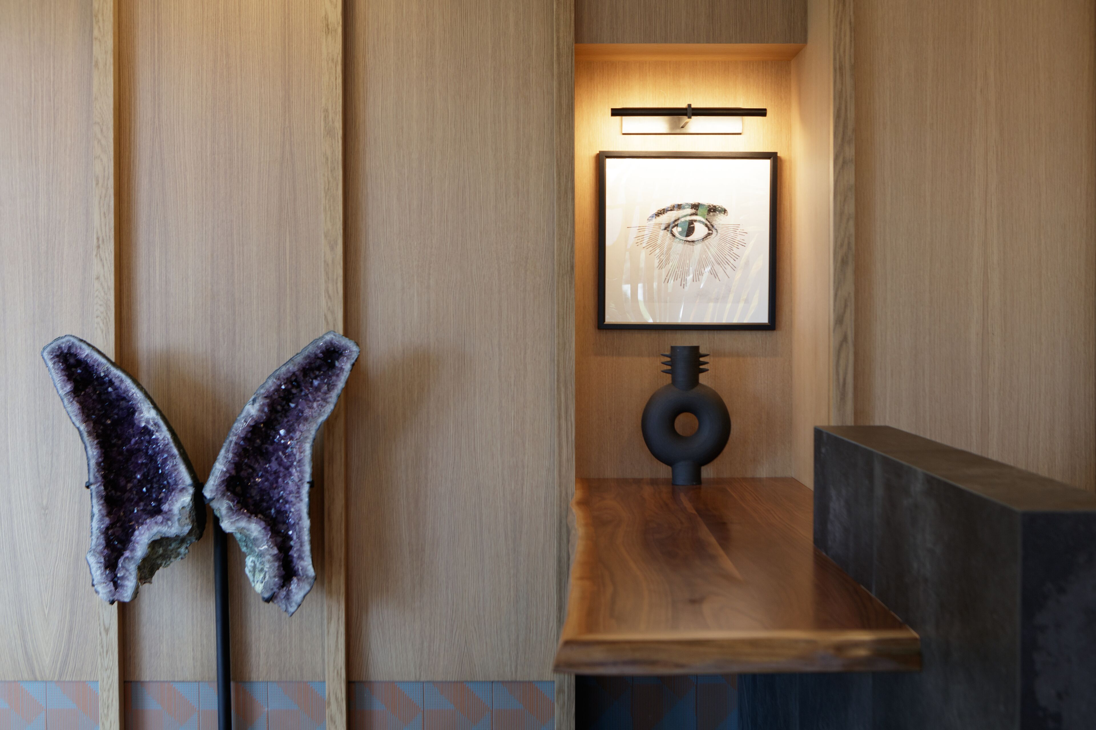 A wooden wall with a framed picture of an eye, a black lamp, and a butterfly decoration.