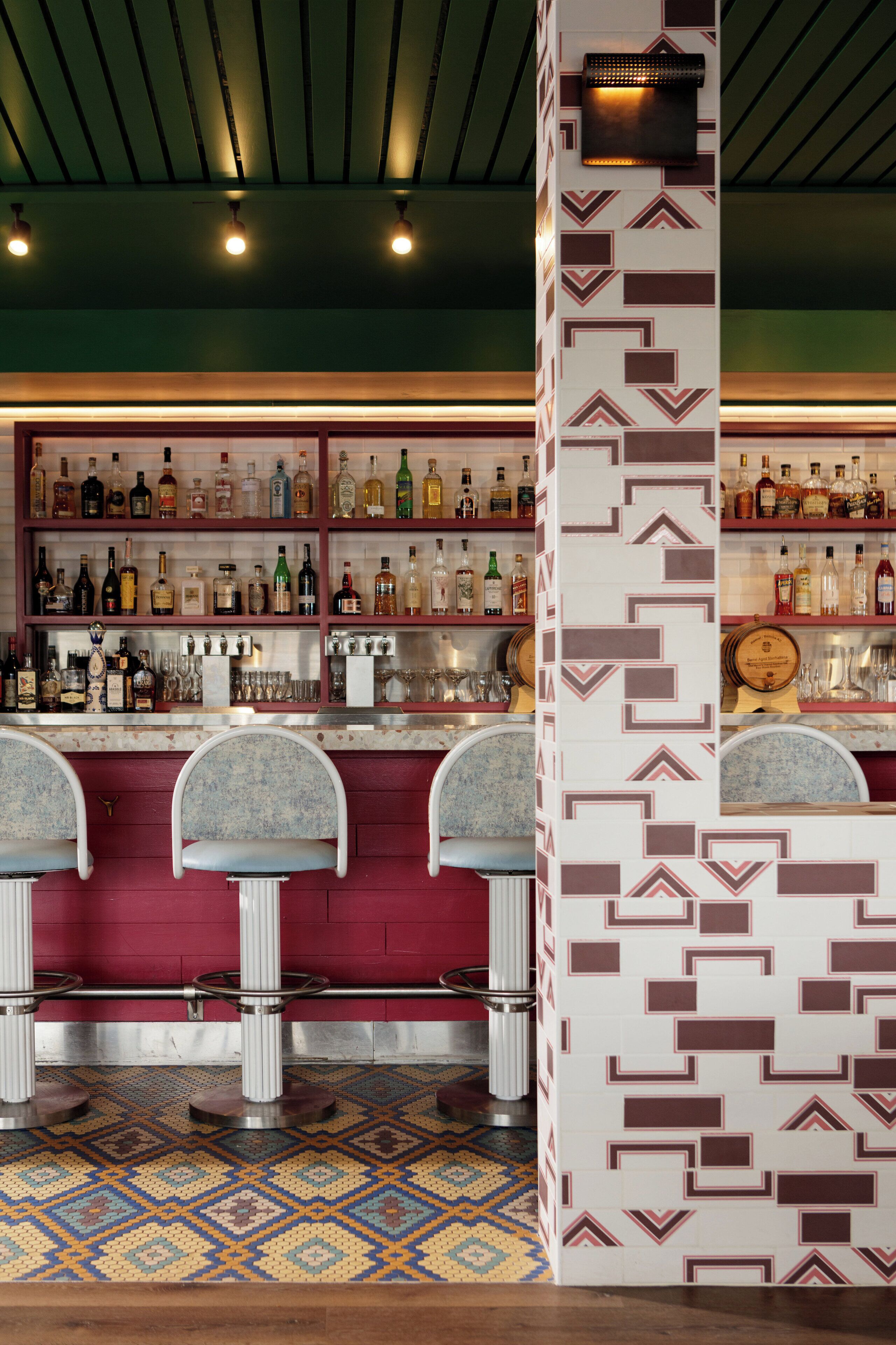 A bar area with multiple shelves of bottles, bar stools, and a patterned wall.