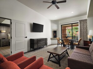 A modern living room with a flat-screen TV, a fireplace, a dining area, and a balcony with curtains.