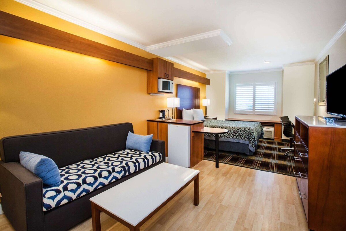 Ein kompaktes Hotelzimmer mit Sofa, Esstisch, Bett, Fernseher und einer Küchenzeile.