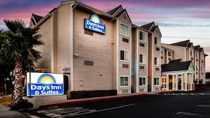 En Days Inn & Suites bygning med skilt, parkeringsplads og palmetræ.