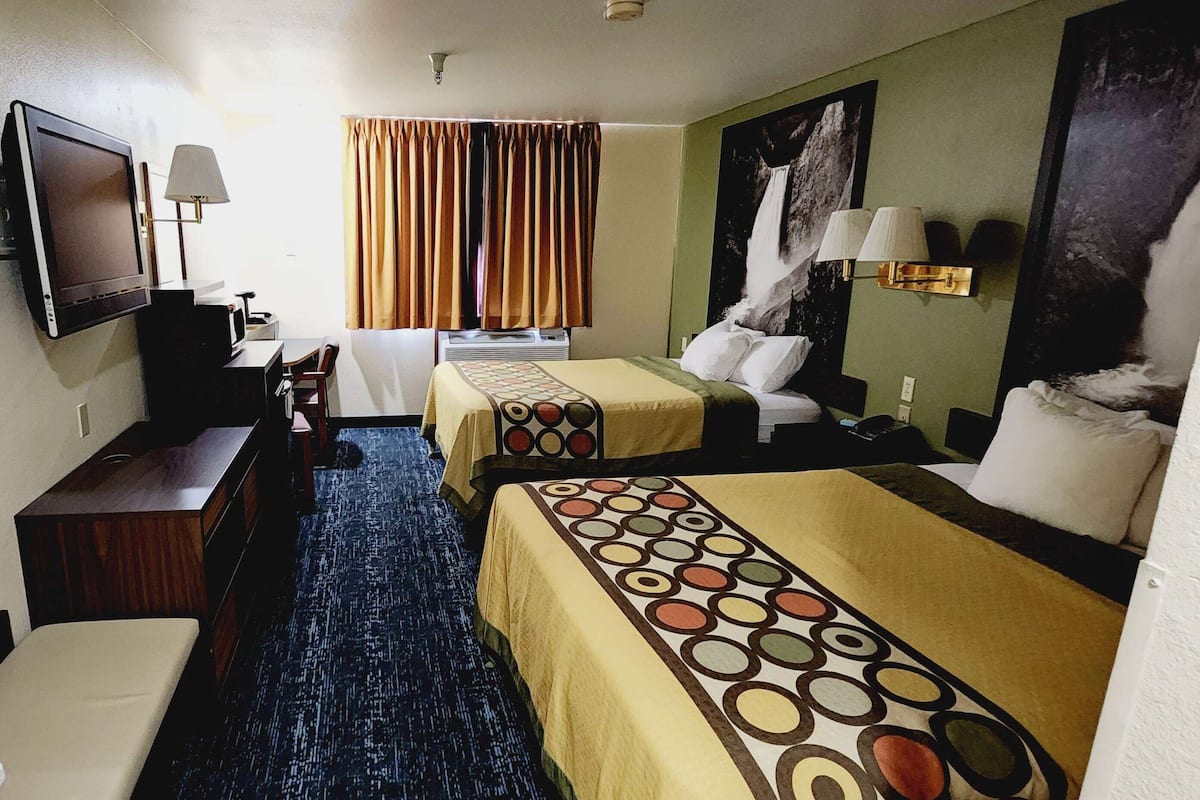 A hotel room with two beds, a TV, a desk, a chair, a lamp, and a painting on the wall.