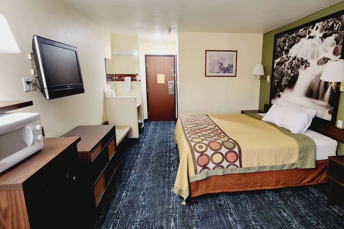 A hotel room with a bed, a desk with a computer, a television, and a bathroom with a mirror and towel rack.