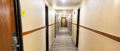A hotel corridor with carpeted floors, doors on both sides, and a ceiling with recessed lighting.