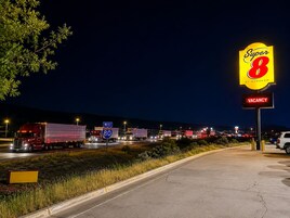 Escena de autopista con un gran letrero de 'Super 8' que indica un motel, un letrero de 'VACANCY' y varios camiones en la carretera.