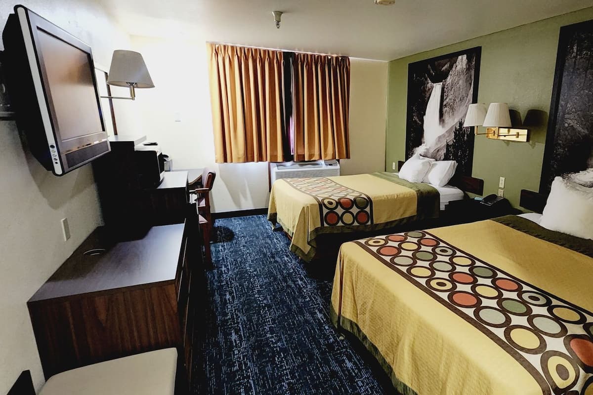 A hotel room with two beds, a desk, a TV, and a large wall painting.