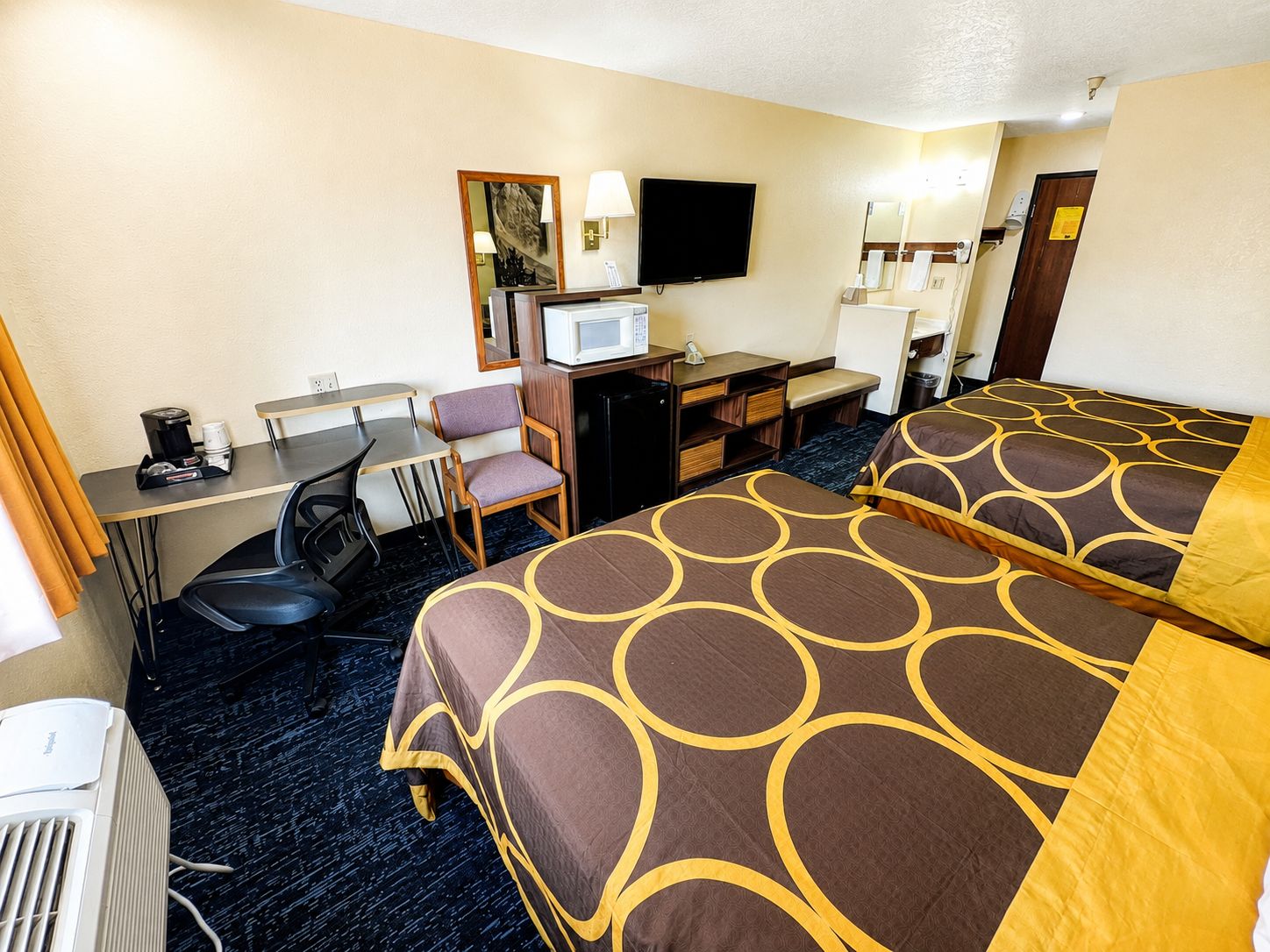 A hotel room with two beds, a desk, a chair, a television, and a microwave.