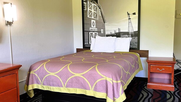 Habitación de hotel con cama, mesita de noche, cómoda y un espejo grande que refleja un granero y un molino.