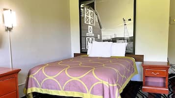 A hotel room with a bed, a nightstand, a dresser, and a large mirror reflecting a barn and windmill.