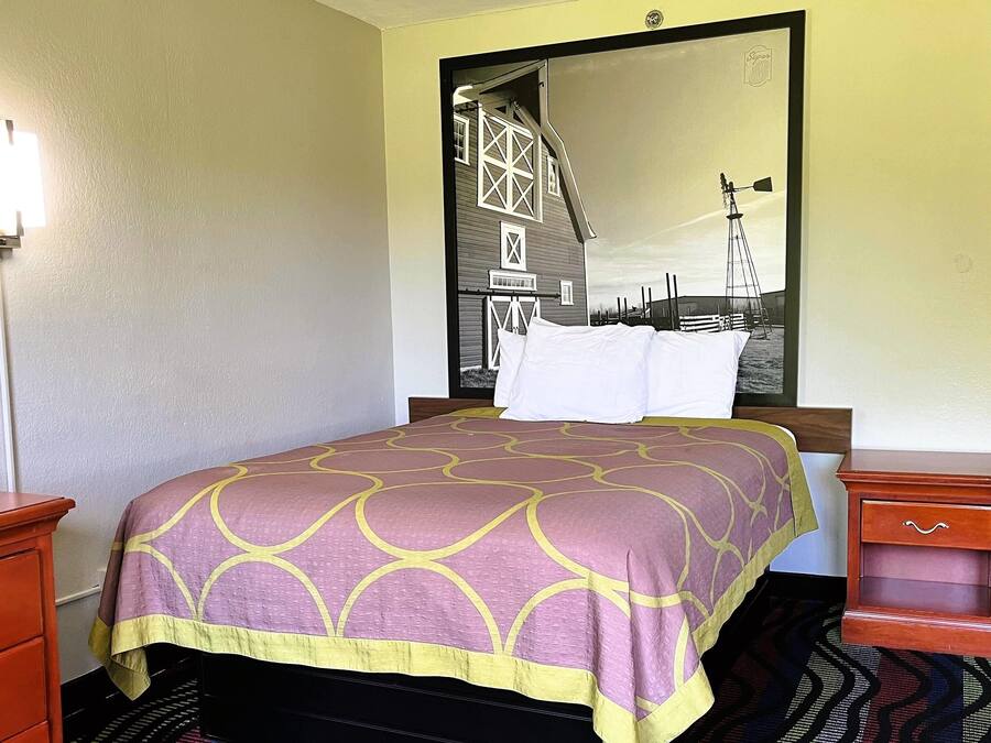 A hotel room with a bed, a nightstand, a dresser, and a large mirror reflecting a barn and windmill.