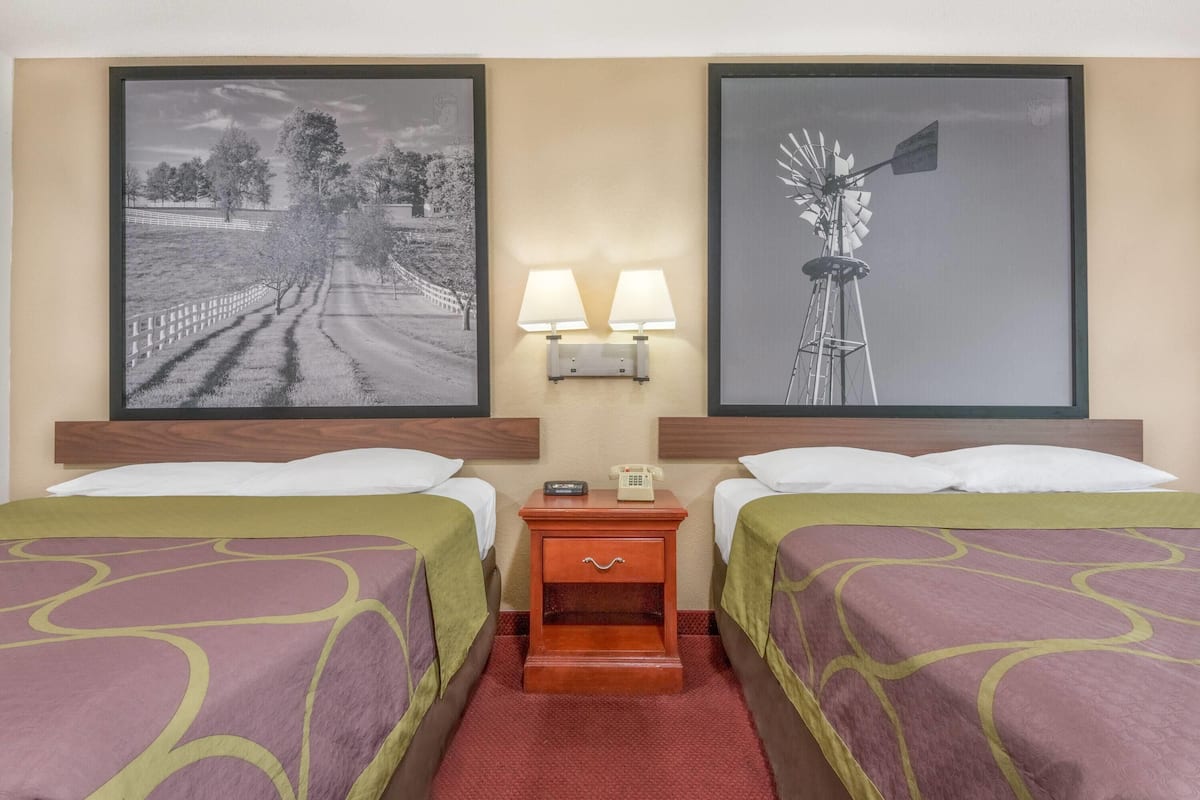 A hotel room with two beds, a nightstand with lamps, and two framed pictures on the wall.