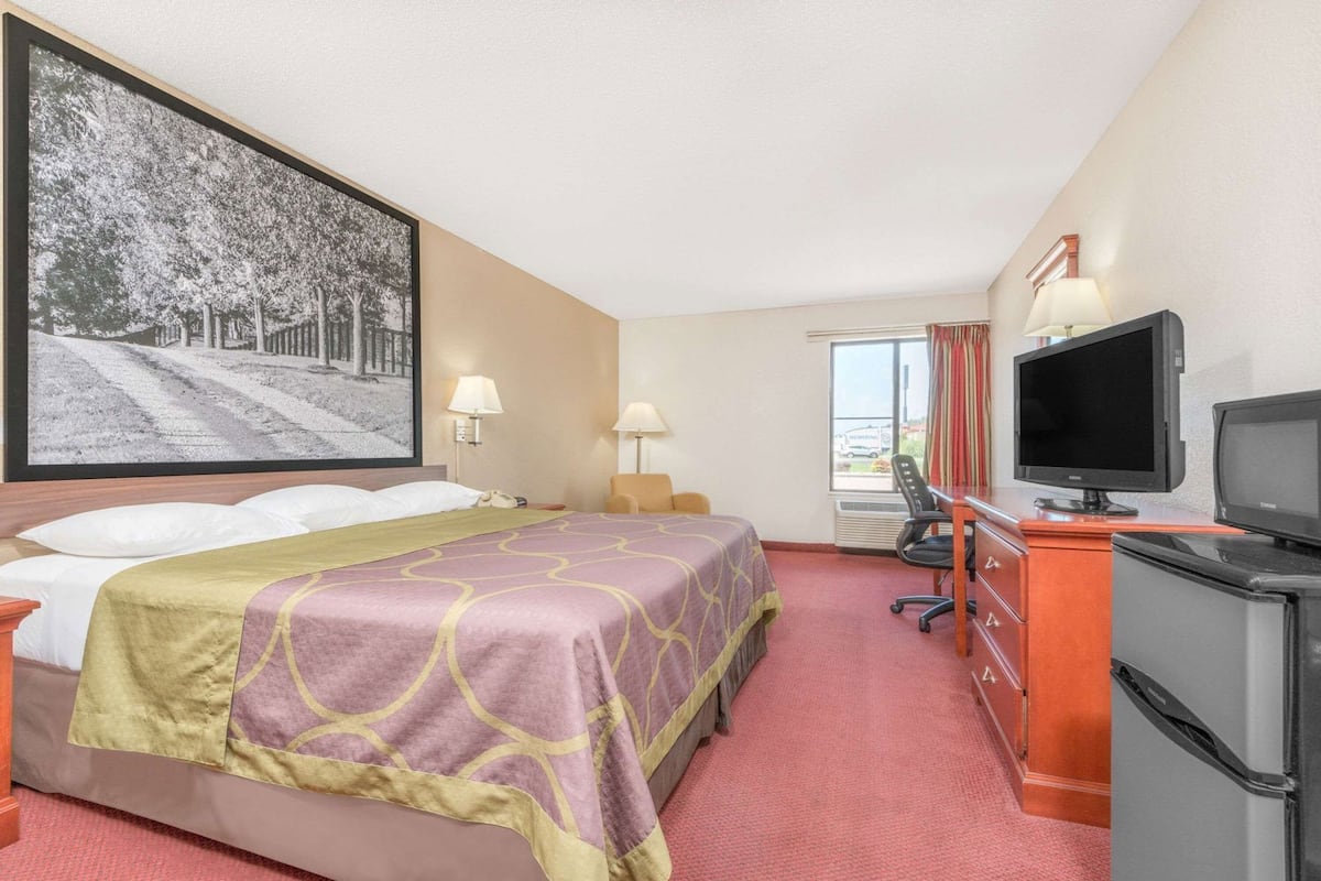 A hotel room with a bed, a desk with a computer, a television, and a large framed picture on the wall.
