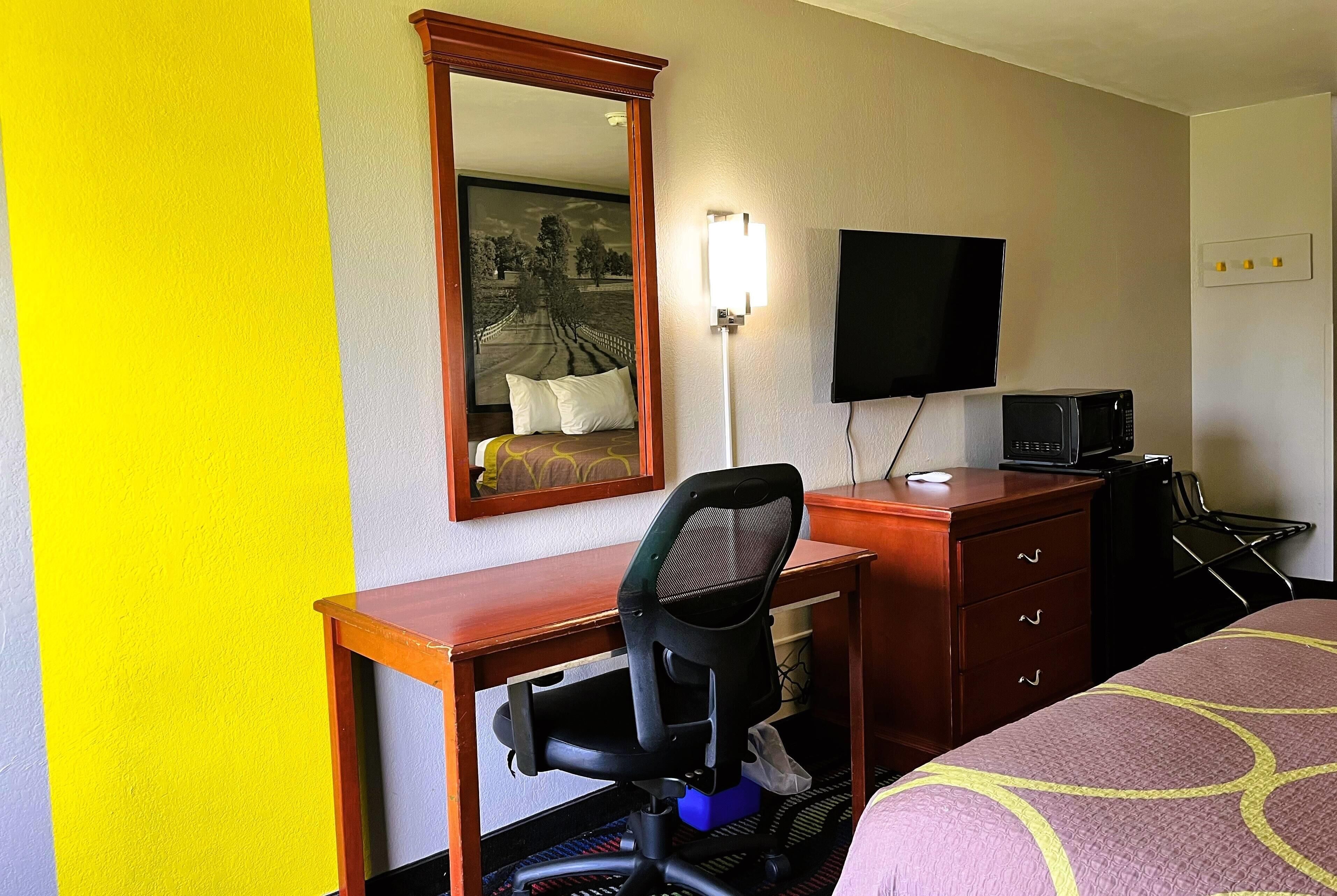 A hotel room with a desk, chair, television, and a bed with a patterned bedspread.