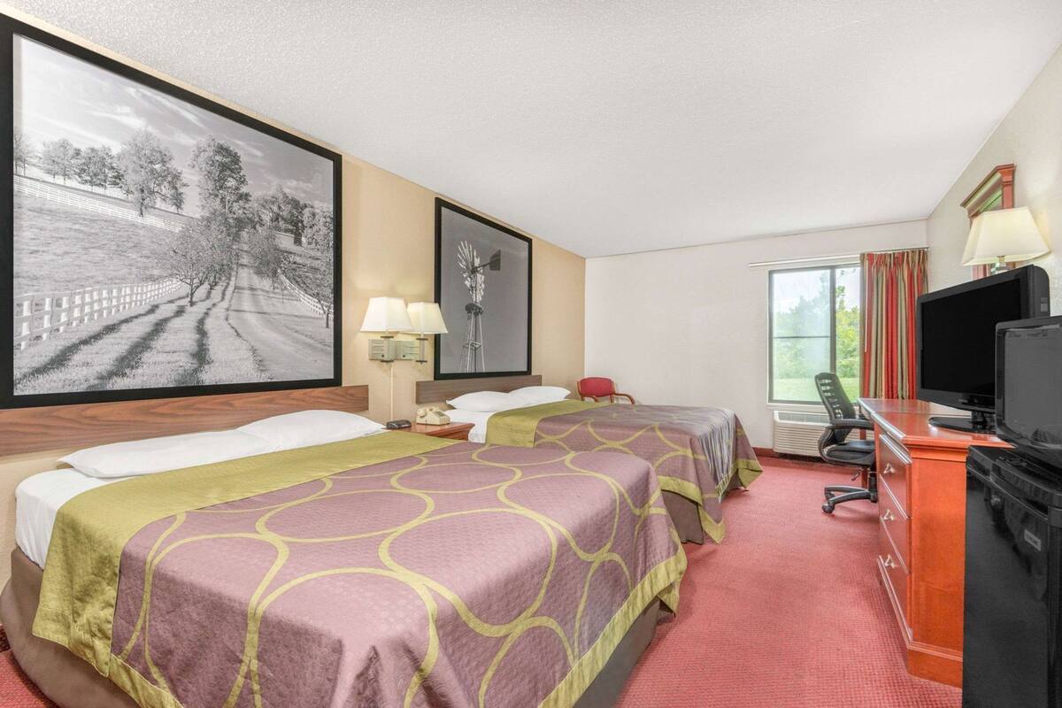 A hotel room with two beds, a desk with a computer, a TV, and a window with curtains.