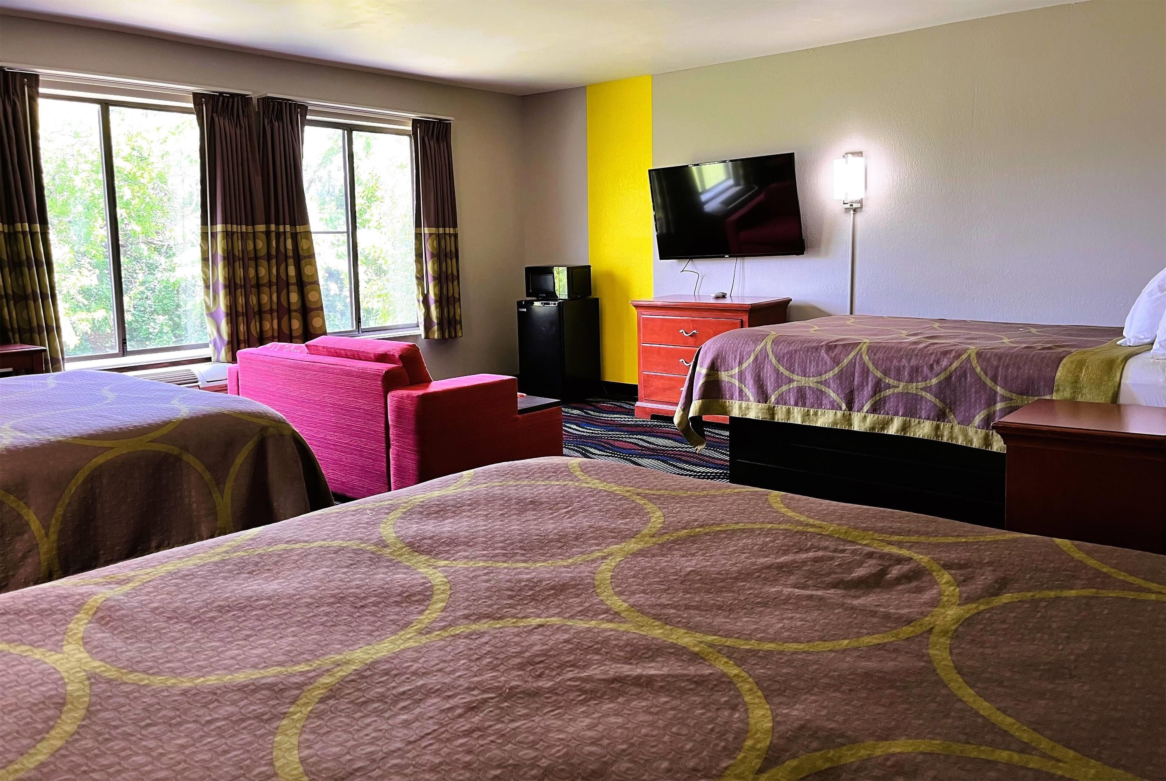 A hotel room with two beds, a TV, a dresser, and a window with curtains.