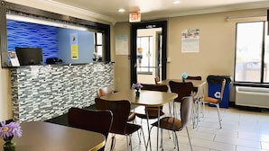 A restaurant with a tiled floor, a blue wall with a wavy pattern, and a reception desk with a computer. There are tables and chairs, and a trash bin with a recycling symbol. - Super 8 by Wyndham Vincennes (Vincennes)