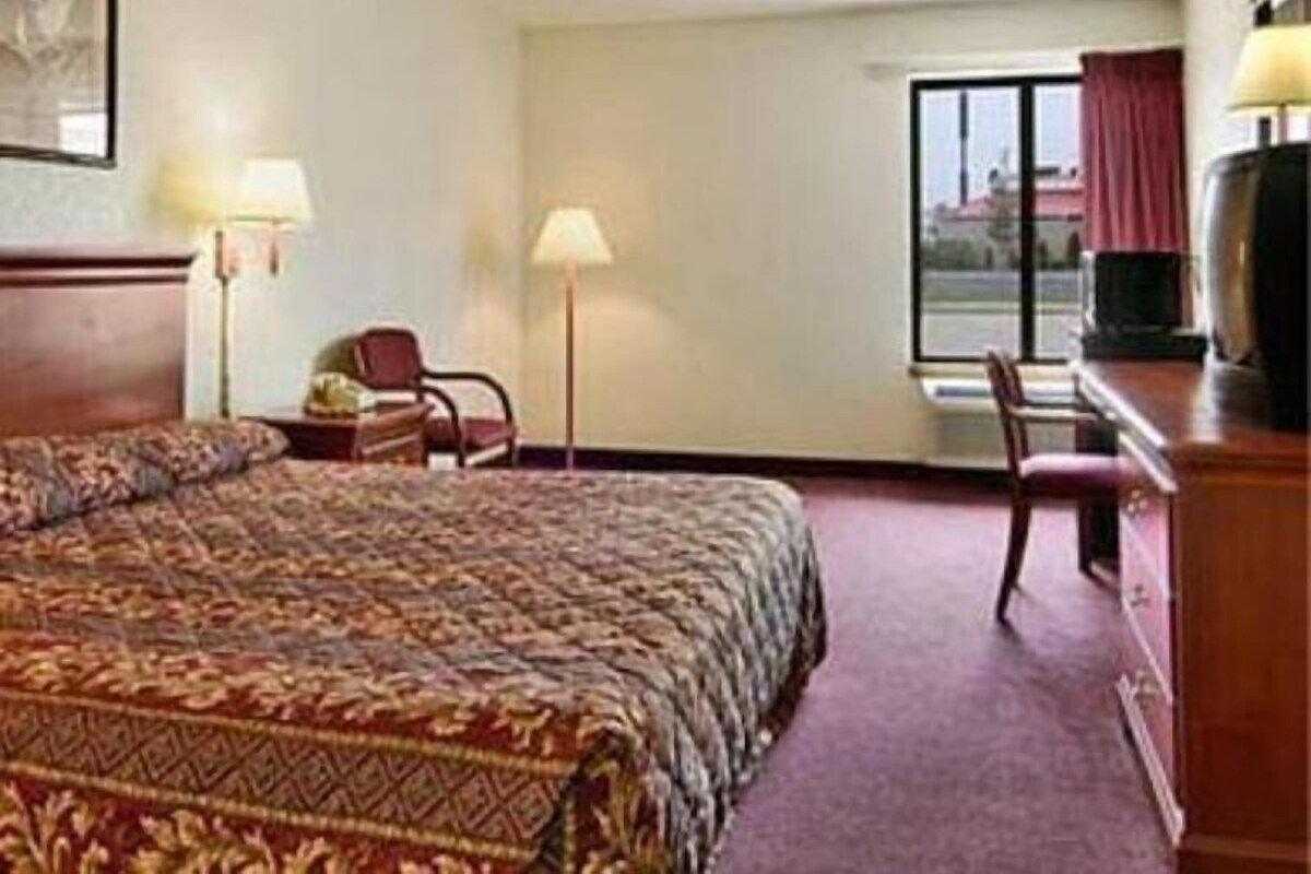 A hotel room with a bed, a desk, a chair, a television, and a window.