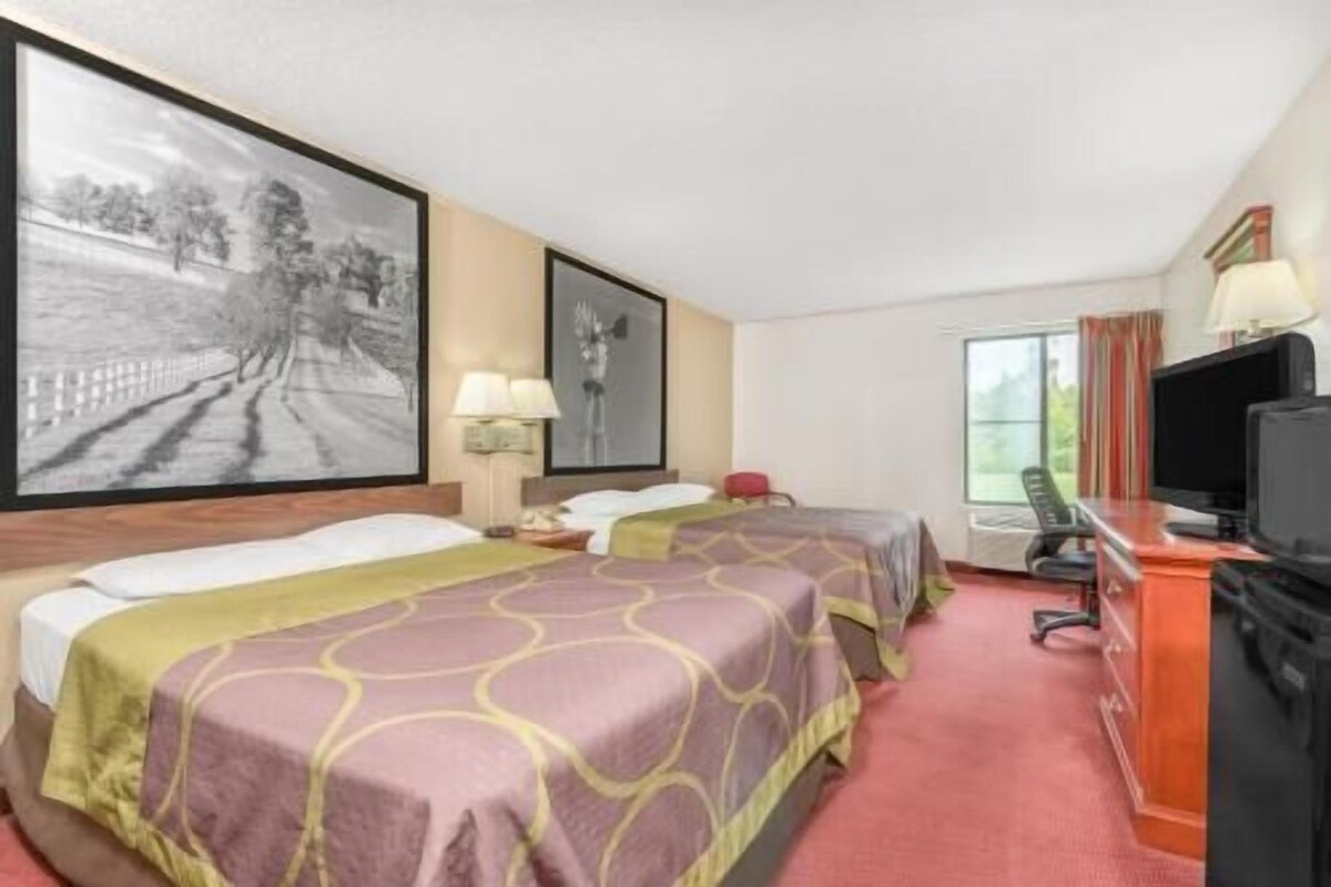 A hotel room with two beds, a desk with a computer, a television, and a large framed picture on the wall.