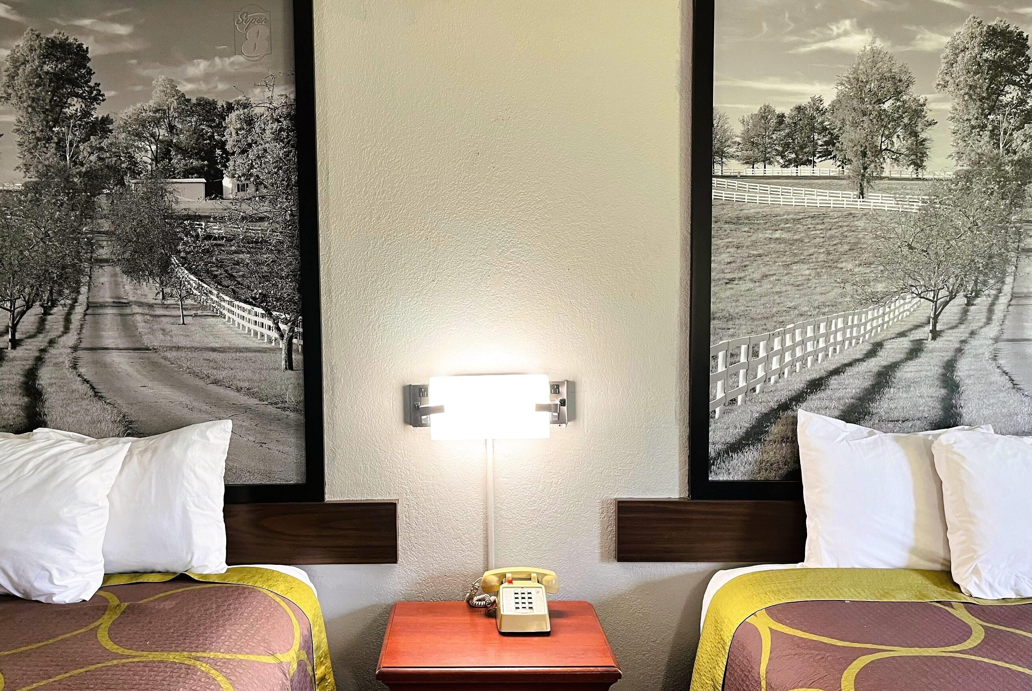 A hotel room with two beds, a nightstand with a telephone, and a wall-mounted light.