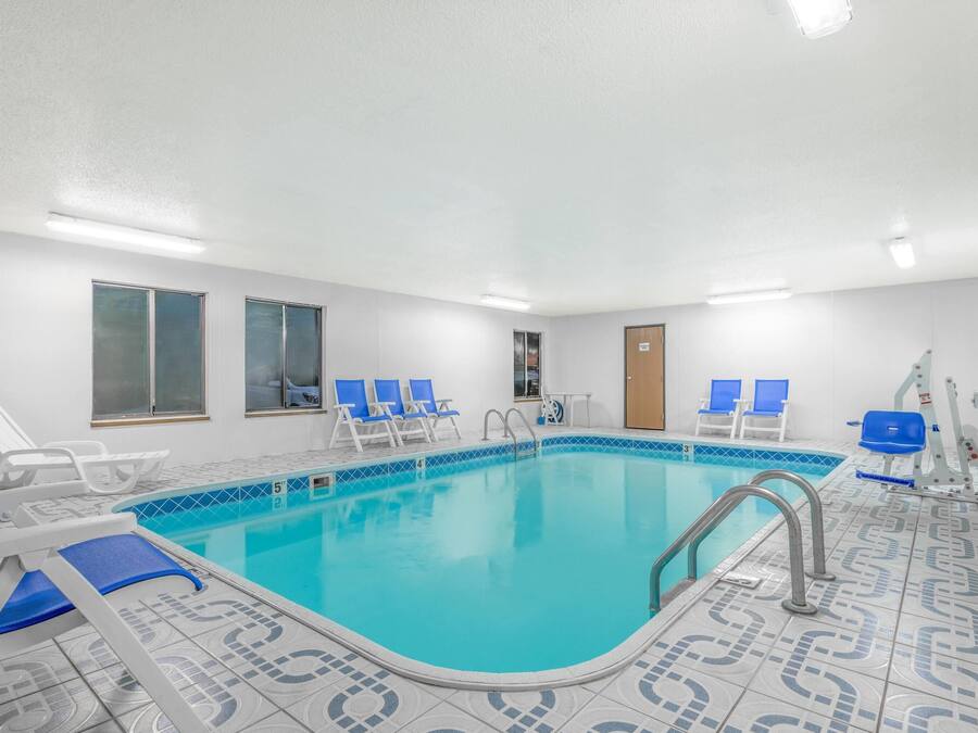 Una piscina con baldosas azules, paredes blancas y sillas de descanso azules.