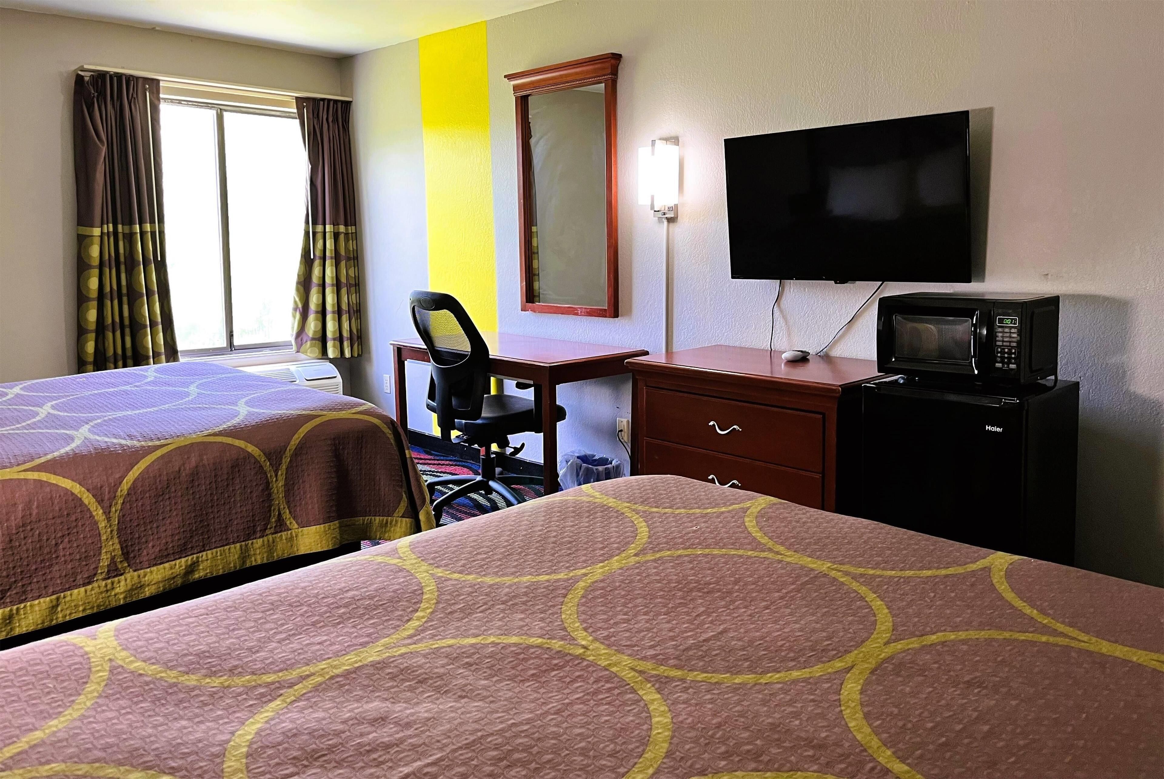 Habitación de hotel con dos camas, un escritorio con silla, televisión, microondas y cómoda.
