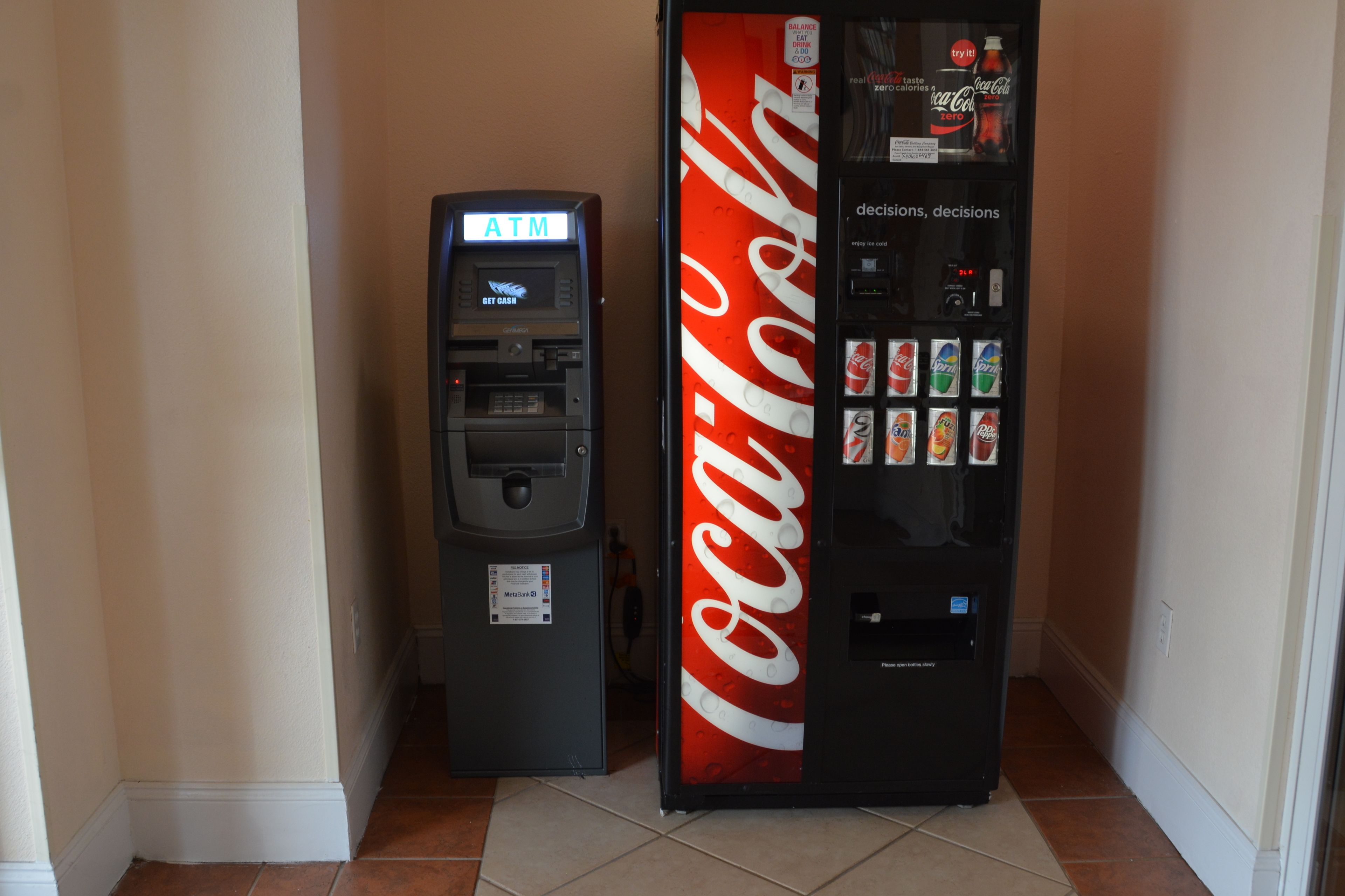 Un cajero automático y una máquina expendedora de Coca-Cola en un pasillo.