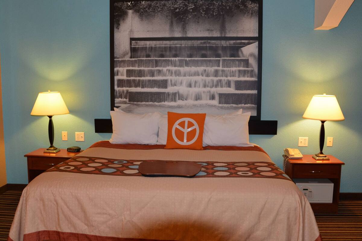 Habitación de hotel con cama, dos mesitas de noche con lámparas, teléfono en la pared y un cuadro grande con una cascada.