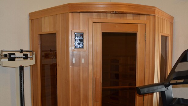 Un sauna en bois équipé d’un panneau de commande, d’un siège noir et d’un appareil de mesure fixé au mur.