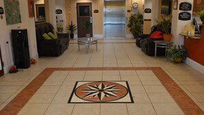 Un hall d’hôtel doté d’un motif géométrique central en mosaïque, d’espaces aménagés pour s’asseoir et d’un comptoir de réception.