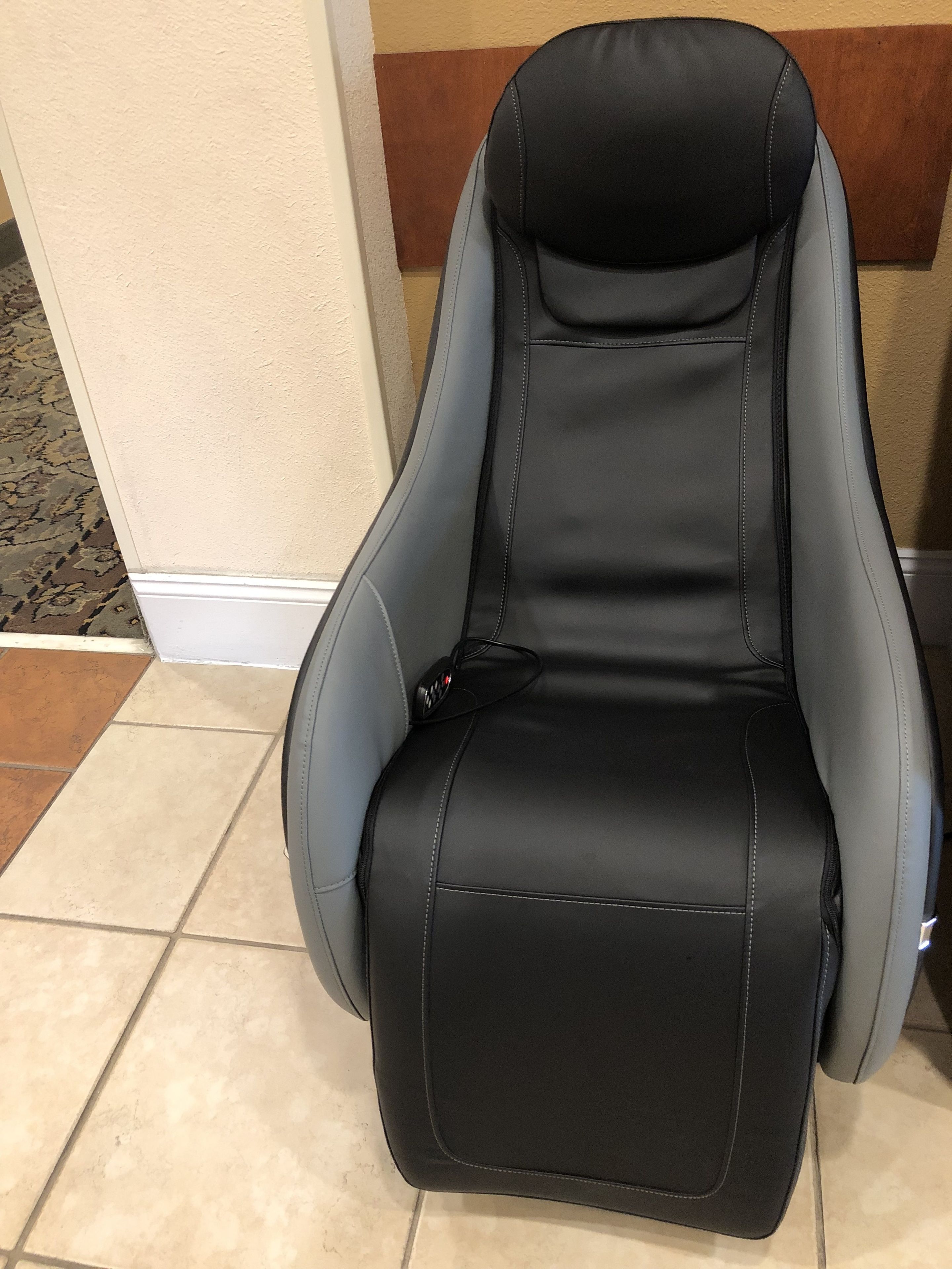 A black and gray office chair with a high backrest and armrests, positioned against a wall with a beige and brown striped pattern.
