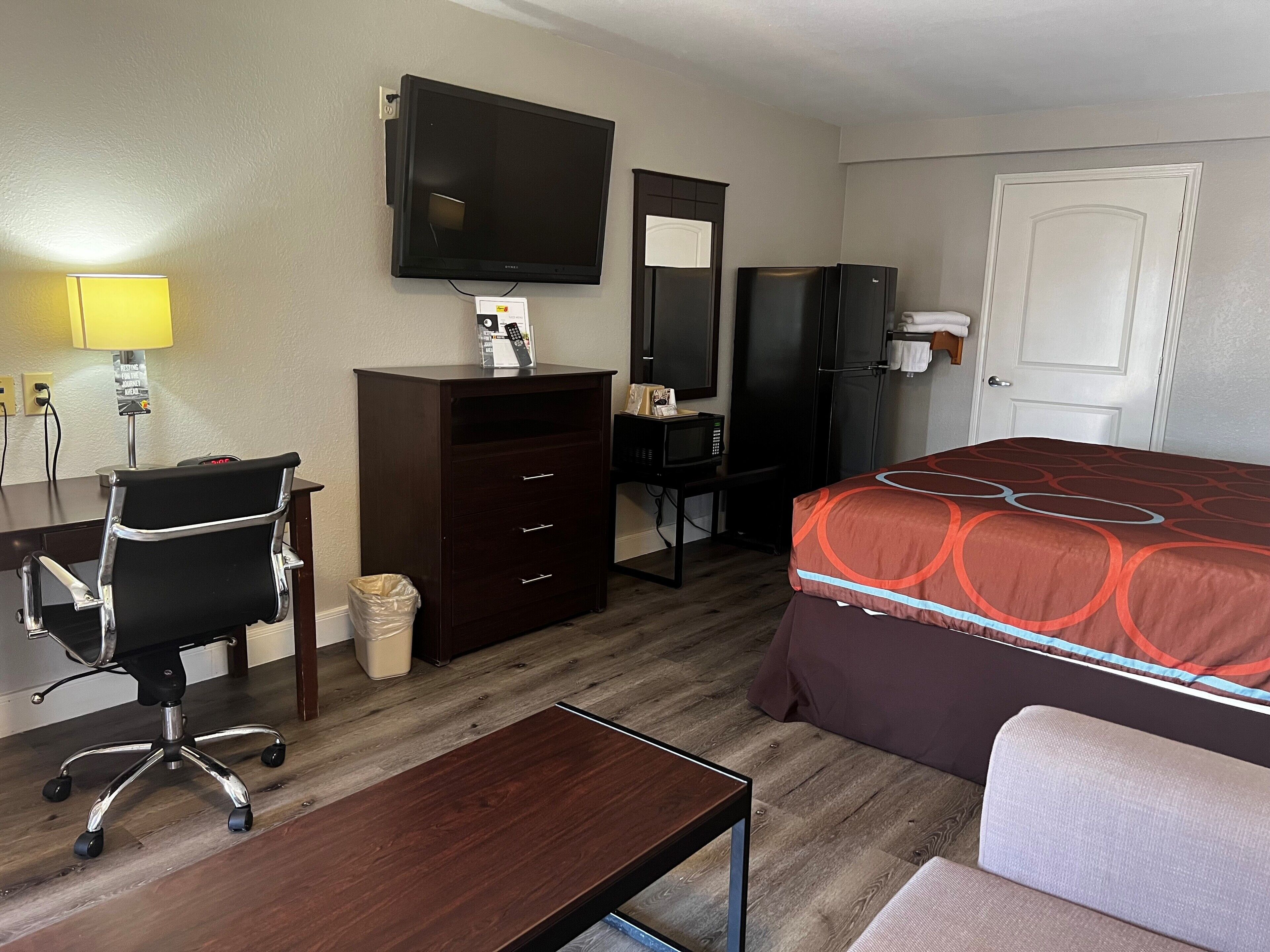 Una habitación de hotel con cama, escritorio, silla, televisor y microondas.
