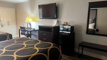 A hotel room with a bed, a desk with a lamp, a TV, a microwave, a dresser, and a mirror.